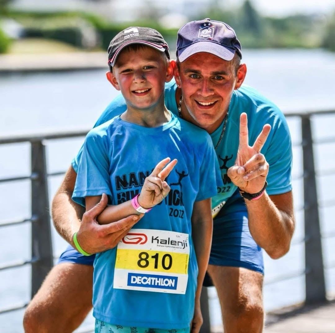 Un père et son fils en t-shirts bleus d'événement, dossard au ventre, à l'arrivée d'une course